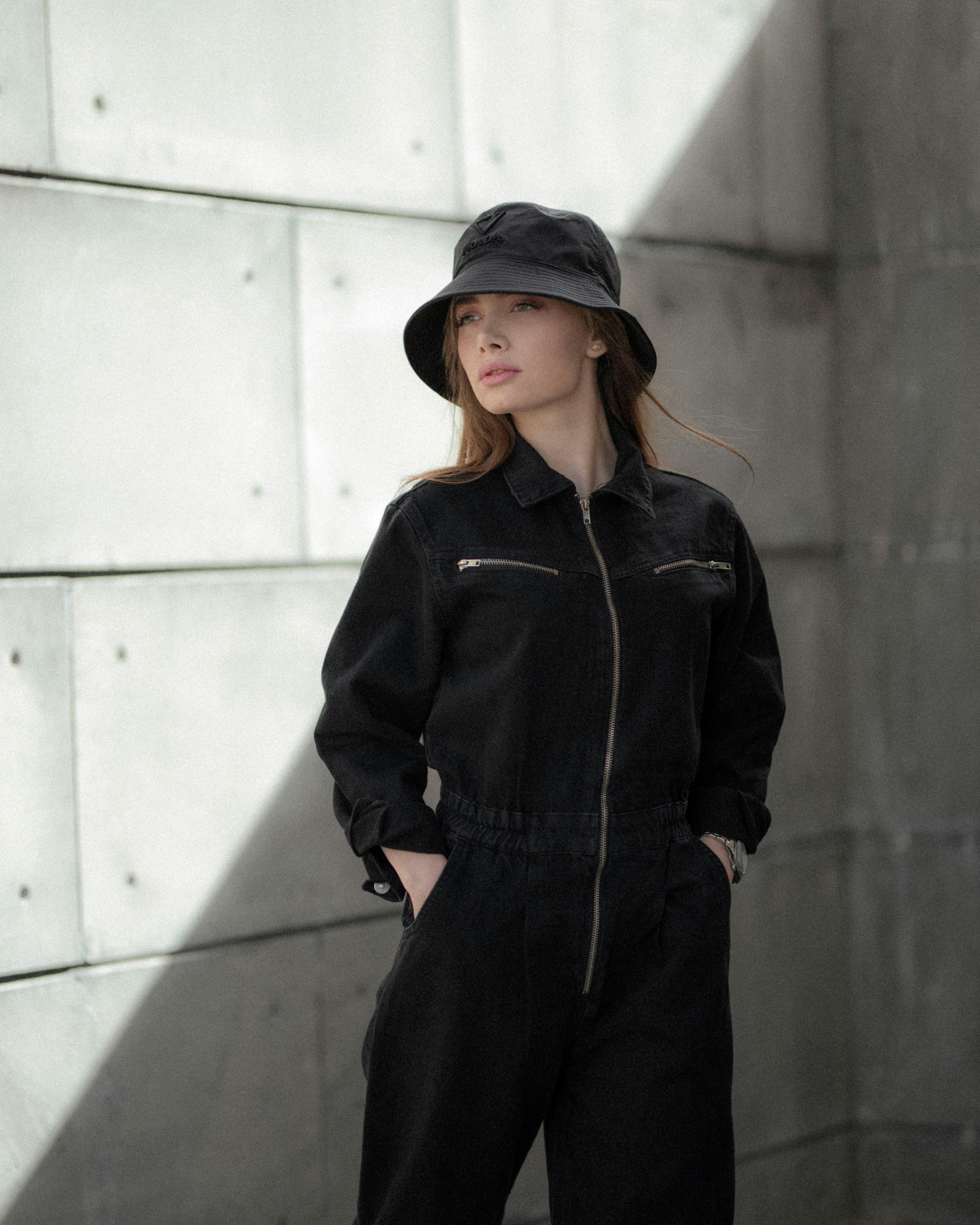 woman in black leather jacket and brown hat standing near white wall